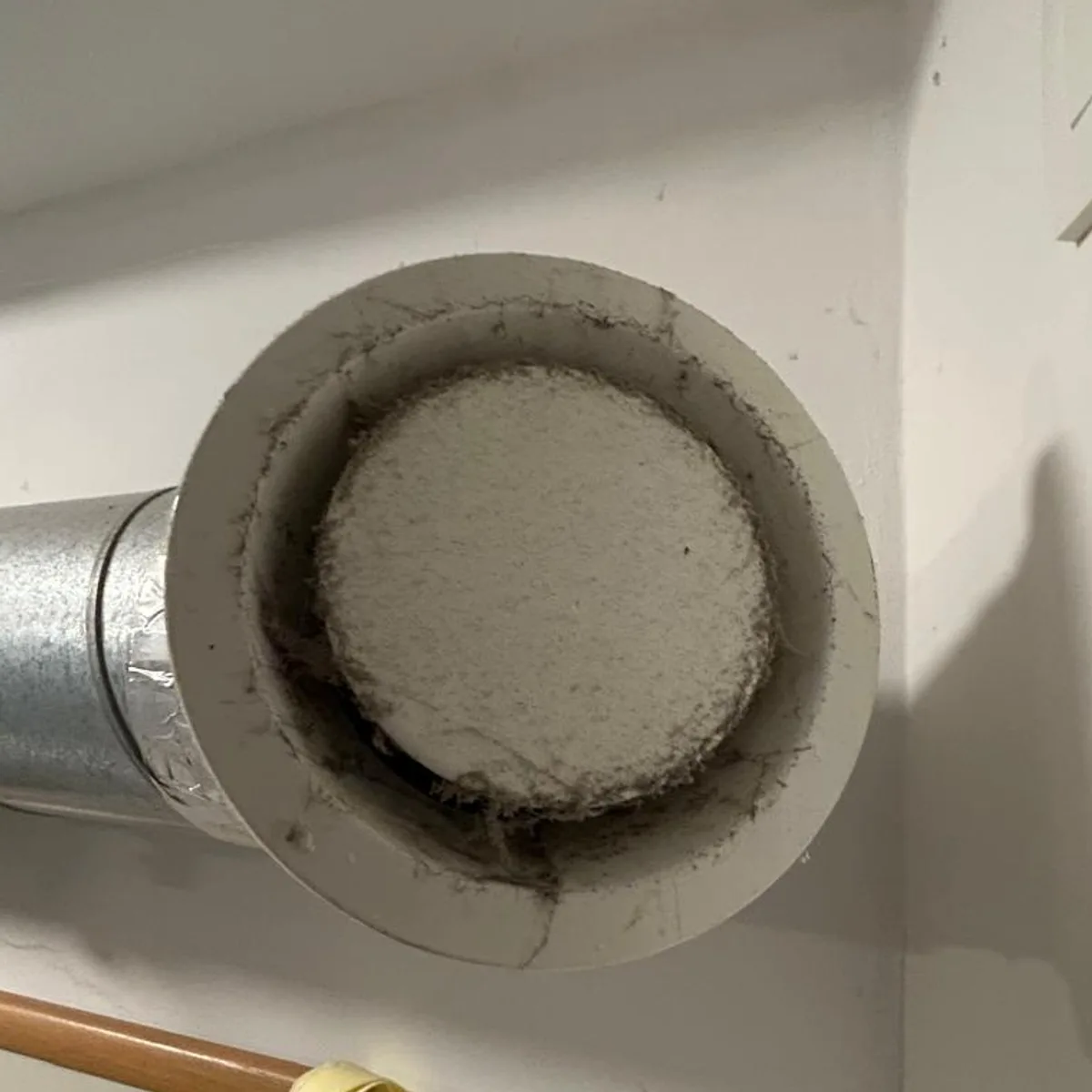 Bouche d'extraction murale ouverte avant l'entretien, filtre et collerette chargés de poussière.