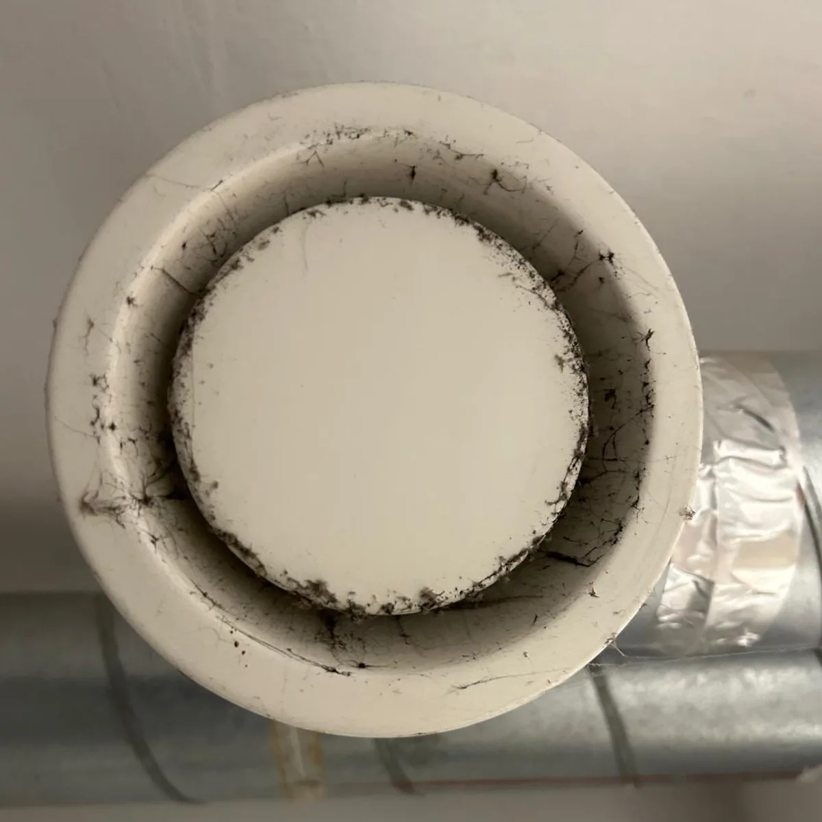 Bouche d'extraction au plafond avant l'entretien : la couronne et le disque sont couverts de poussière grise et de fibres.
